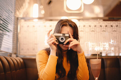 Teenage girl photographing with vintage camera while sitting in cafe - CAVF78004
