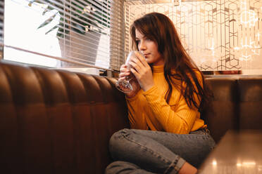 Nachdenkliche junge Frau trinkt Schokoladenmilchshake in einem Café am Fenster - CAVF78005