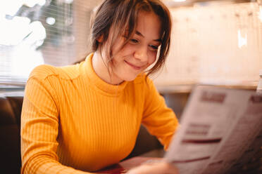 Happy teenage girl looking at menu while sitting in cafe - CAVF78009