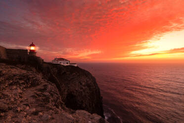 Küstenlandschaft bei Sonnenuntergang mit rötlichem Himmel und einem beleuchteten Leuchtturm am Kap von San Vicente, Portugal - CAVF78024