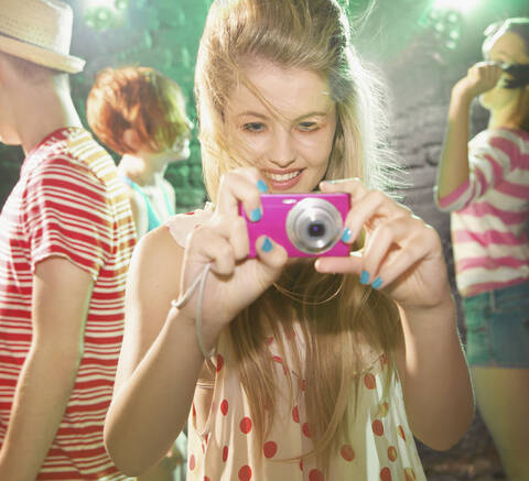 Verspieltes Teenager-Mädchen mit Digitalkamera auf einer Party, lizenzfreies Stockfoto