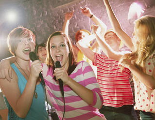 Happy teenage friends singing karaoke at party - FSIF04647