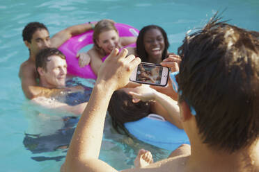 Teenage boy with camera phone photographing friends in swimming pool - FSIF04664