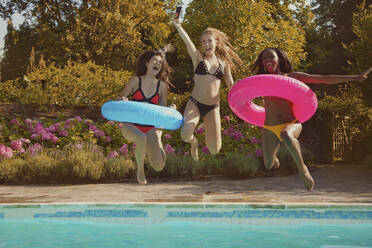 Playful teenage girl friends jumping into sunny summer swimming pool - FSIF04666
