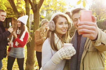 Happy teenage couple taking selfie with smart phone in autumn park - FSIF04677