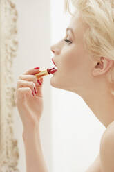 Profile glamorous young woman applying red lipstick - FSIF04684