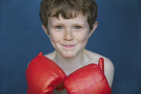 Porträt lächelnder Junge mit Sommersprossen in Boxhandschuhen - FSIF04687