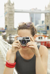 Porträt einer jungen Frau mit Retro-Kamera vor der Tower Bridge, London - FSIF04693