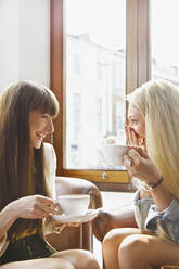 Glückliche junge Frauen trinken Kaffee in einem Caféfenster - FSIF04695