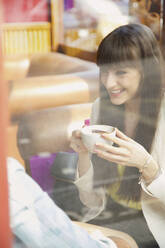 Glückliche junge Frau genießt einen Cappuccino im Caféfenster - FSIF04697