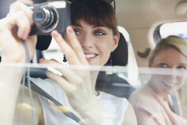 Happy young woman using digital camera from car window - FSIF04702