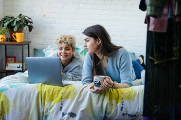 Freundinnen schauen auf den Laptop, während sie sich zu Hause auf dem Bett entspannen - CAVF78051