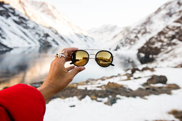 Ein Tourist hält in den Bergen eine modische Sonnenbrille hoch - CAVF78090