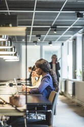 Geschäftsfrau arbeitet an einem Laptop, während sie mit einem Kollegen im Büro sitzt - MASF17569