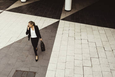 High angle view of businesswoman talking through phone while walking on street - MASF17604