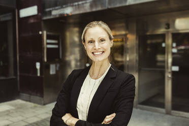 Portrait of confident female entrepreneur with arms crossed standing against building - MASF17606