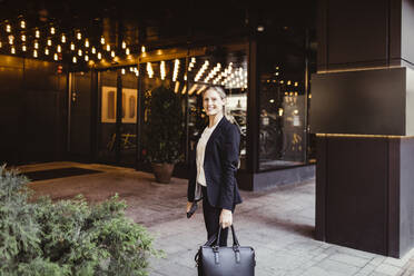 Porträt einer Unternehmerin mit Tasche, die am Eingang eines Gebäudes steht - MASF17607