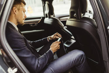 Side view of businessman using smart phone while sitting in car - MASF17612