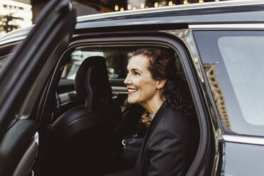 Lächelnde Unternehmerin schaut beim Aussteigen aus dem Auto weg - MASF17617