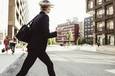 Geschäftsfrau mit Smartphone beim Überqueren der Straße - MASF17623