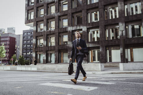 Männlicher Unternehmer, der beim Überqueren der Straße nach oben schaut - MASF17626