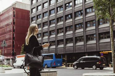 Unternehmerin mit Smartphone, die gegen ein Gebäude läuft - MASF17660