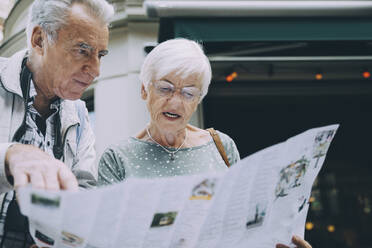 Senior woman reading map while standing with partner in city during vacation - MASF17663