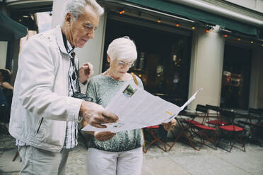 Senior couple reading map while standing on sidewalk in city during vacation - MASF17667
