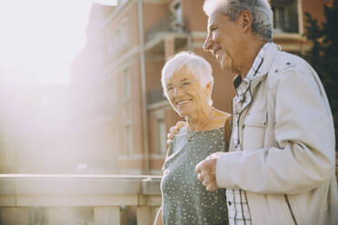 Smiling elderly couple with arm around walking in city on sunny day - MASF17671