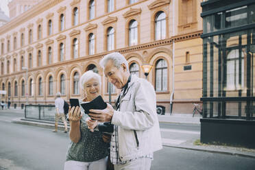 Smiling senior male and female tourist using smart phone while exploring in city - MASF17675