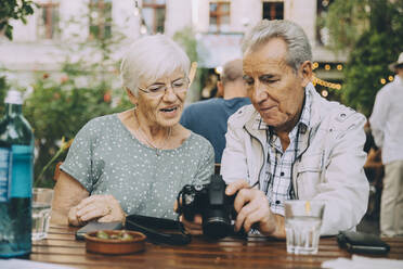 Ein älterer Mann zeigt einer Frau in einem Restaurant in der Stadt seine Kamera - MASF17678