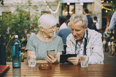 Retired couple using mobile phone while sitting at restaurant in city - MASF17679