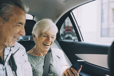 Lächelndes Rentnerpaar, das im Urlaub im Auto sitzend ein Mobiltelefon benutzt - MASF17687