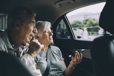 Ältere Frau hält Mobiltelefon, während sie mit einem Mann im Auto sitzt - MASF17688