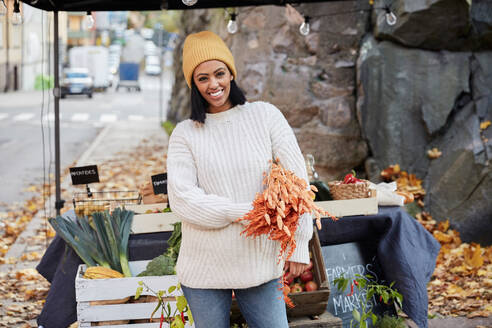 Porträt einer glücklichen Frau mit Feldfrüchten an einem Marktstand - MASF17720