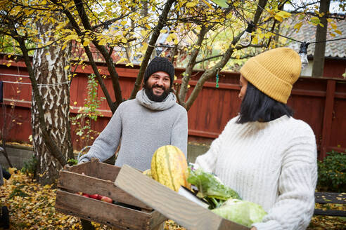 Ein lächelnder Mann und eine Frau unterhalten sich, während sie einen Korb mit frischem Gemüse im Garten halten - MASF17724