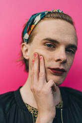 Portrait of confident young man touching cheek while standing against pink background - MASF17791