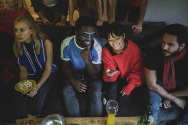 Männlich und weiblich, die ihr Smartphone benutzen, während sie mit Freunden auf dem Sofa zu Hause sitzen - MASF17809