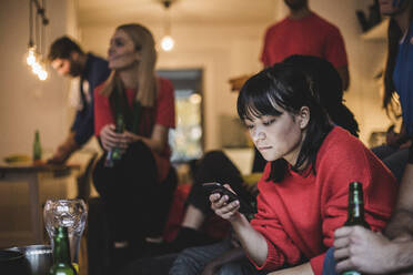 Junge Frau benutzt ein Mobiltelefon, während sie mit Freunden zu Hause sitzt - MASF17812