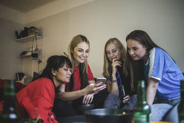 Smiling female friends using mobile phone while sitting at home - MASF17816