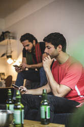 Männliche Fußballfans nutzen ihr Mobiltelefon, während sie zu Hause ein Spiel ansehen - MASF17822