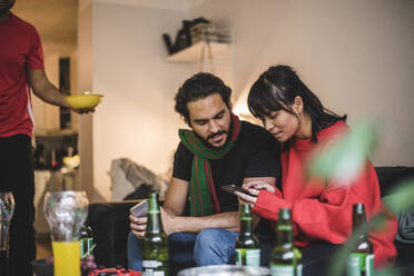Männliche und weibliche Freunde benutzen ihr Smartphone, während sie zu Hause ein Spiel ansehen - MASF17823