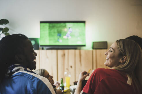 Lächelnder Mann und lächelnde Frau schauen Fußball, während sie mit Freunden zu Hause sitzen - MASF17833