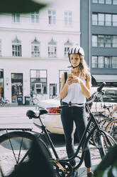 Geschäftsfrau mit Helm, die ein Mobiltelefon benutzt, während sie auf der Straße in der Stadt steht - MASF17842