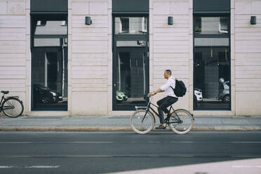 Full length of businessman riding bicycle on street against building in city - MASF17846