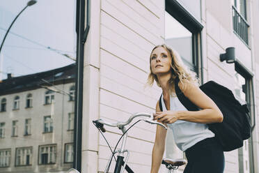 Weibliche Führungskraft mit Fahrrad vor einem Gebäude in der Stadt stehend - MASF17849