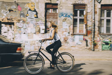 Side view of young businesswoman riding bicycle against building in city - MASF17852