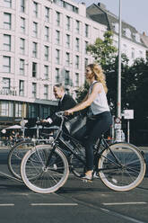 Male and female coworkers riding on street bicycle against building in city - MASF17853