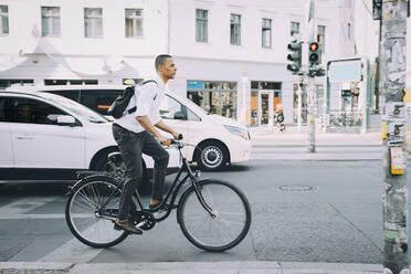 Fahrrad fahrender Geschäftsmann in voller Länge auf dem Bürgersteig vor einem Gebäude in der Stadt - MASF17854