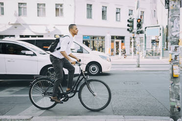 Full length of businessman riding bicycle on sidewalk against building in city - MASF17854